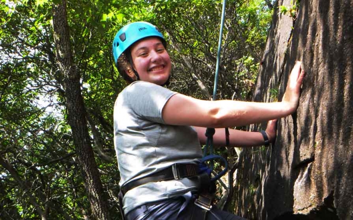a student pauses to smile at the camera while rock climbing on an outdoor leadership course for lgbtq teens
